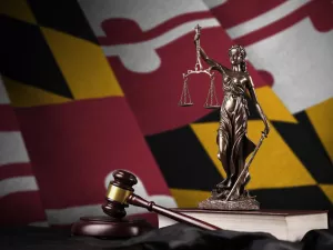 Maryland state flag with statue of lady justice and judge gavel on black drapery