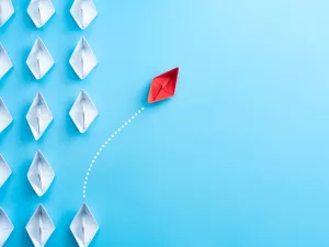 White paper ships on a blue background with a single red ship sailing away unique