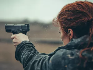 Woman with hair pulled back aiming a gun down range