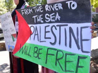 Protestor holding a sign that reads "From the River to the Sea, Palestine will be free"