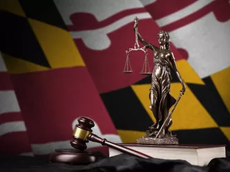 Maryland state flag with statue of lady justice and judge gavel on black drapery