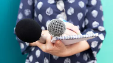 Journalist holding a microphone and writing in a notebook