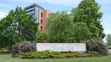 University of Wisconsin Oshkosh sign surrounded by bushes and trees.