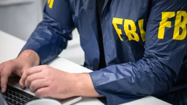 Man in FBI jacket looking at laptop