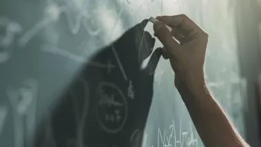 Professor writing mathematical formulas on the chalkboard, hand close up