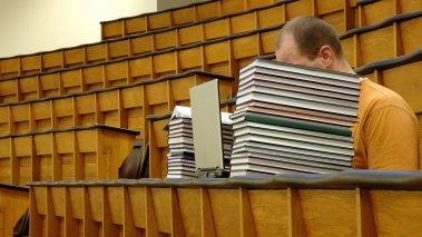 Student in lecture hall with face hidden behind books and laptop