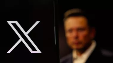 Twitter X logo in close-up with Elon Musk's figure blurred in the background in 2023