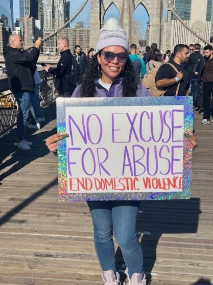 Woman holding sign that reads "No excuse for abuse" at feminist protest on Brooklyn Bridge