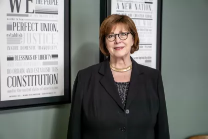 Iowa pollster J. Ann Selzer standing in front of framed newspapers