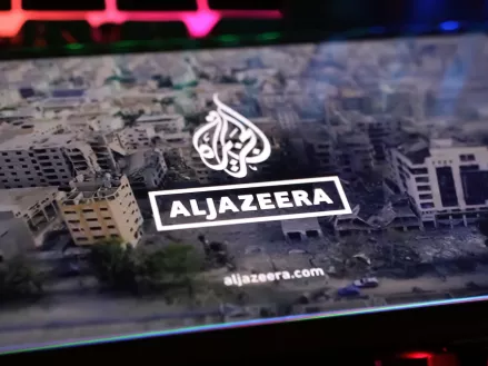 Smartphone screen on computer keyboard with logo lettering of Al Jazeera arabic television with Gaza Israel conflict report 