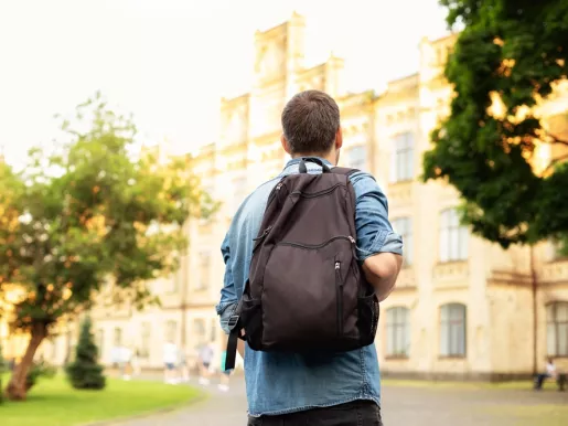 Student university standing with his back to the camera and his backpack on one shoulder and walking in university campus