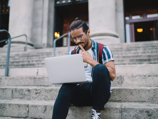 College student on steps looking at laptop