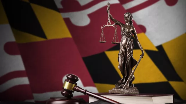 Maryland state flag with statue of lady justice and judge gavel on black drapery